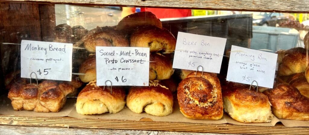 Array of ready to eat savory and sweet buns and filled croissants behind pane at the farmers stand